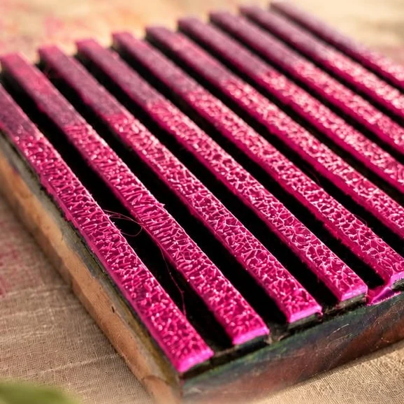A hand-carved print block, inked in magenta, resting on raw jute